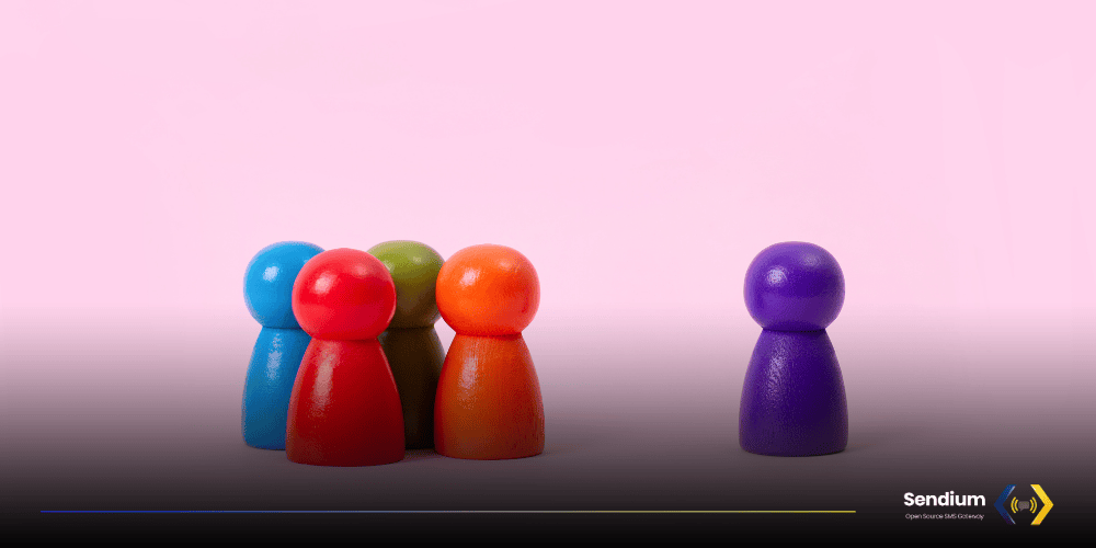 A tight group of four colorful wooden peg dolls stands opposite a single purple peg doll on a pink gradient background, with the Sendium Open Source SMS Gateway logo in the bottom right corner. The dolls emulates the users of the Sendium Community.